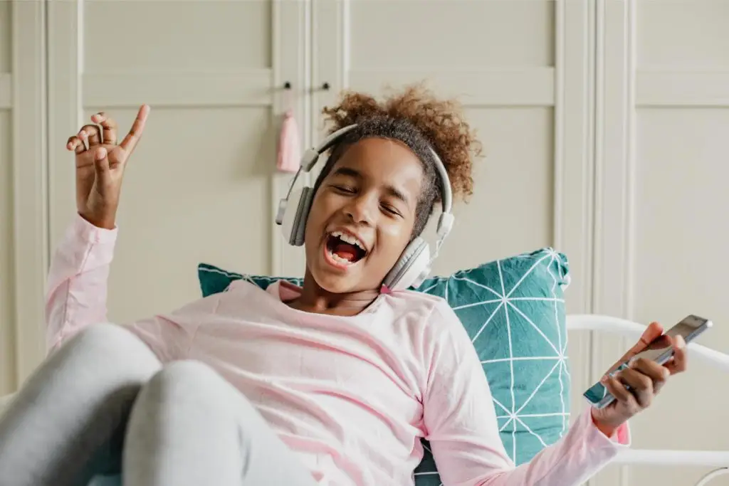 African American girl enjoying free time at home while sitting on the bed and listening to music with headphones