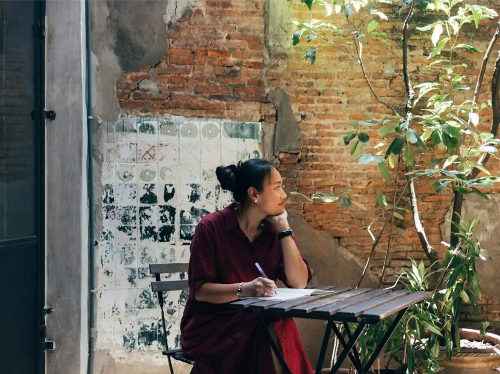A pensive Asian female looking away while thinking about what to write in her diary.