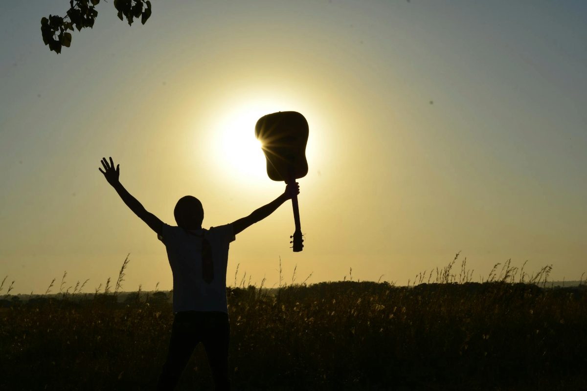 Silhouette of person raising a guitar at sunset in a field, symbolizing music therapy and emotional healing.