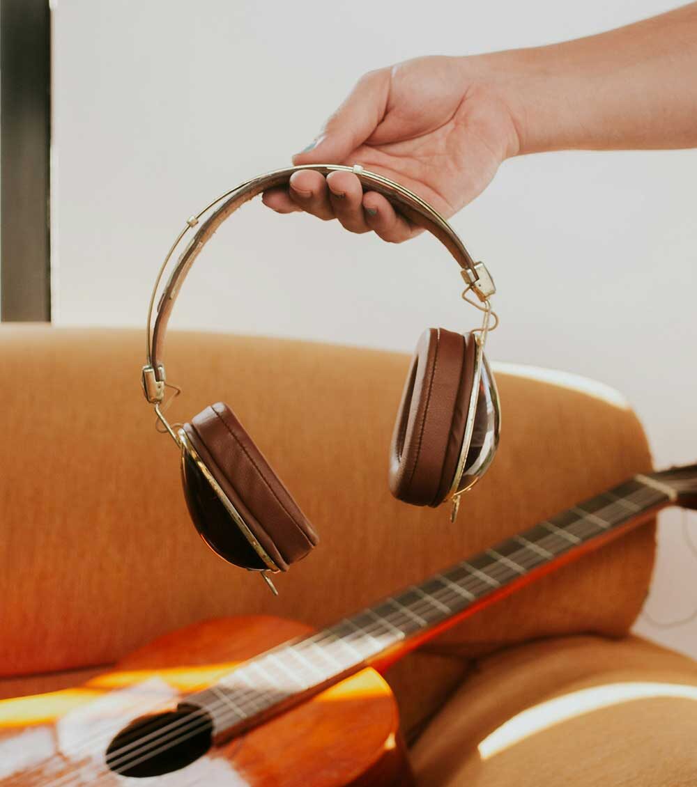 Hand holding vintage headphones above a guitar.