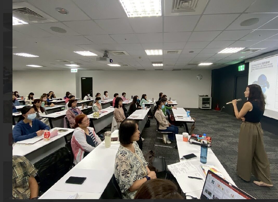 Smiling woman with red glasses and headphones in a greenhouse.