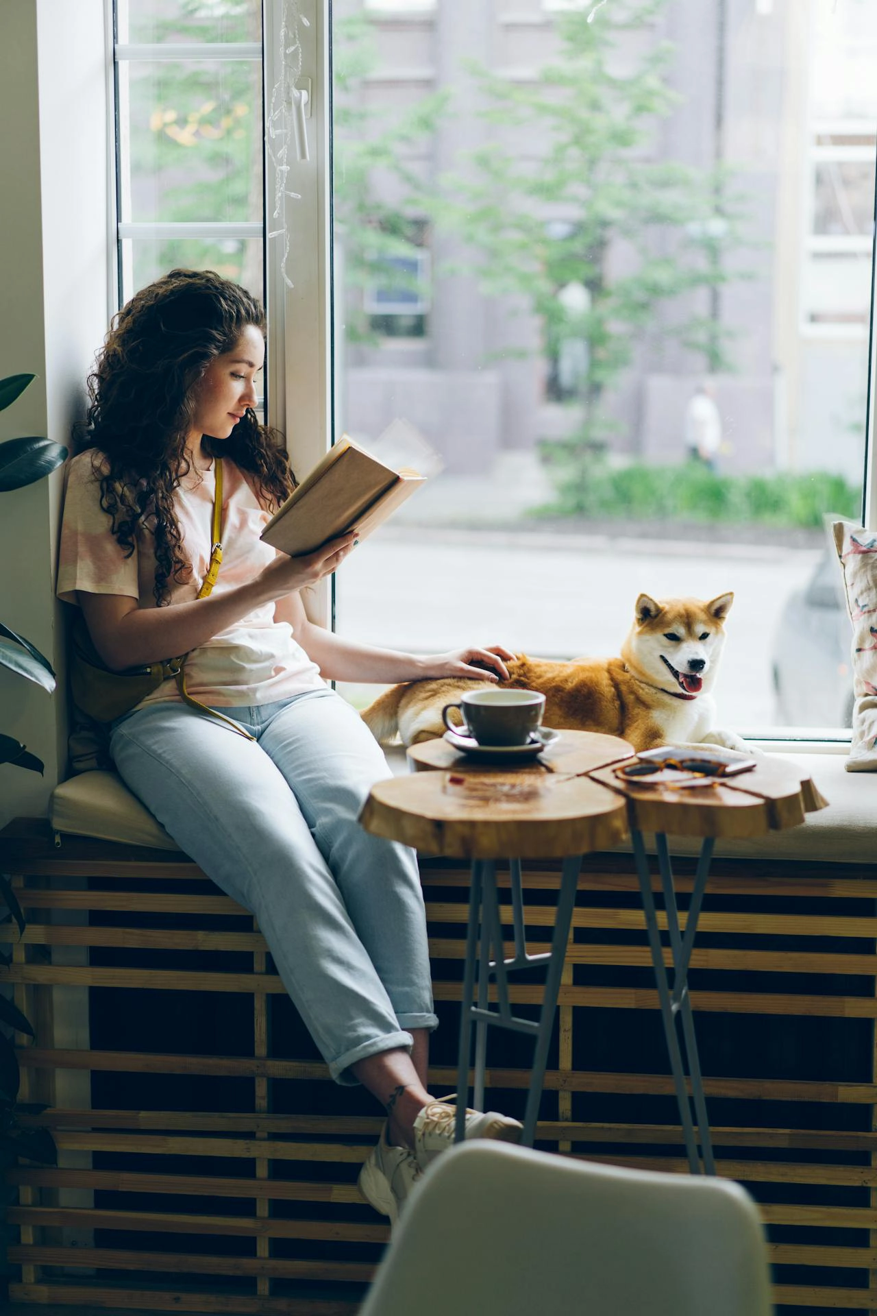 woman sitting in front of window with her dog and reading book