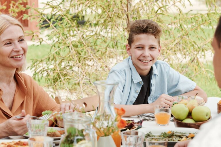 Smiling teen sitting with family during an outdoor meal, showing positive parent-teen connection
