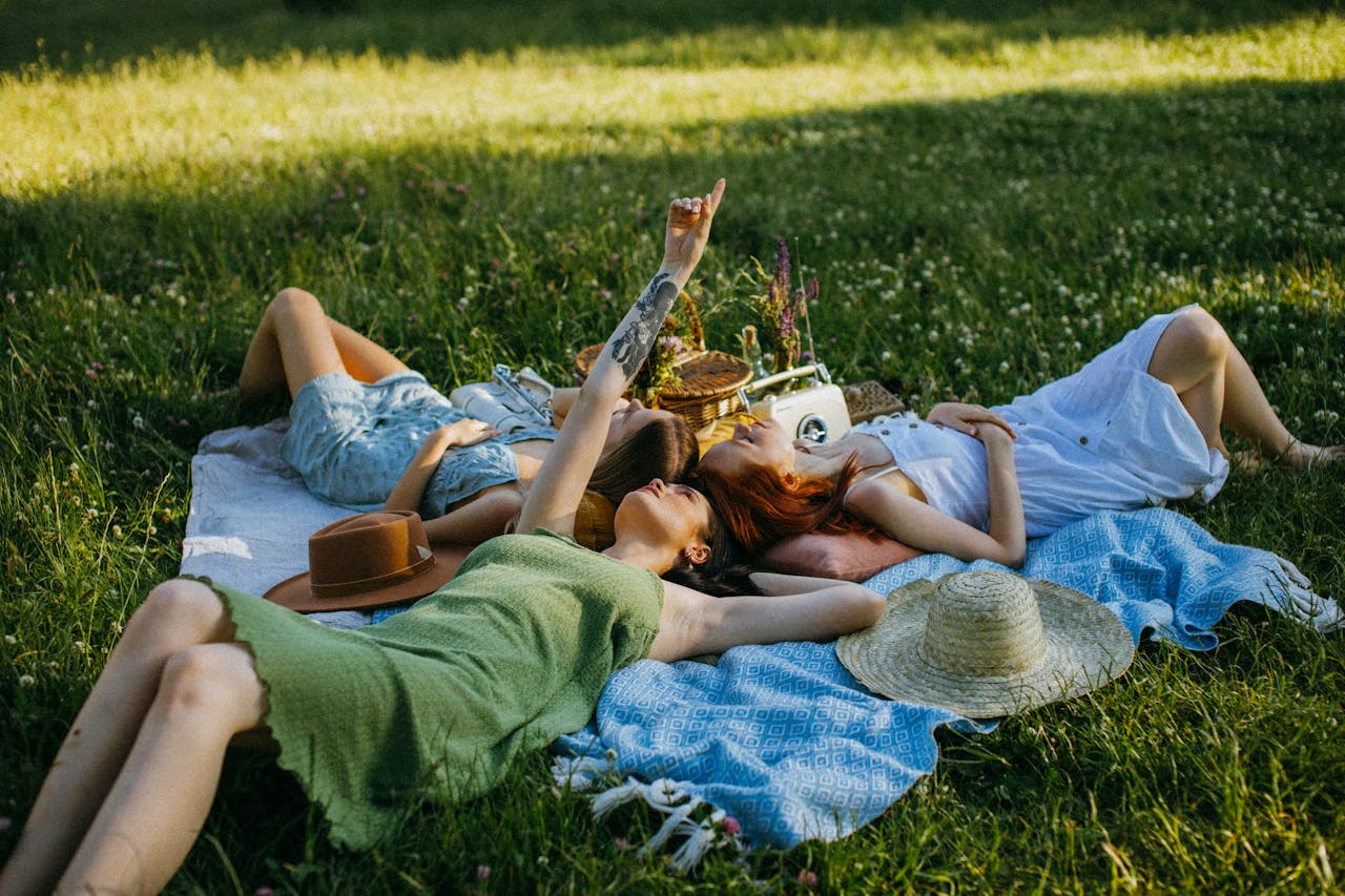 Three women relaxing on a blanket outdoors in a peaceful grassy field, symbolizing comfort, bonding, and emotional safety in a group setting.
