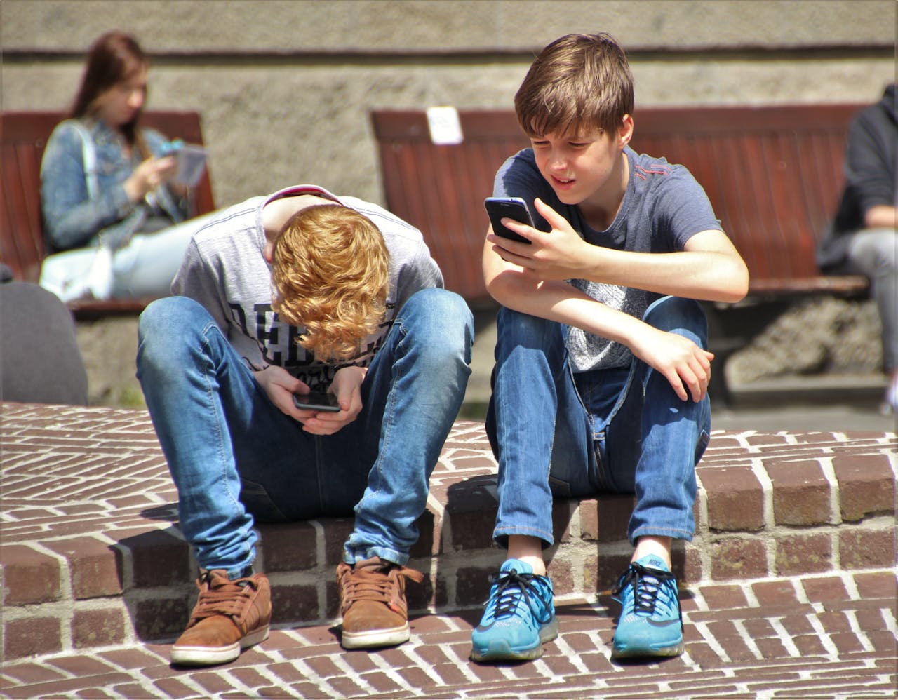 Two teenage boys sitting outside focused on their phones, showing possible social withdrawal