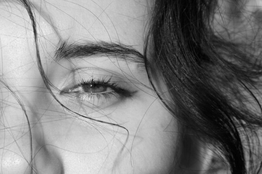 A close-up black-and-white photo of a person’s eye with loose hair strands, representing trauma awareness and EMDR therapy in Austin.