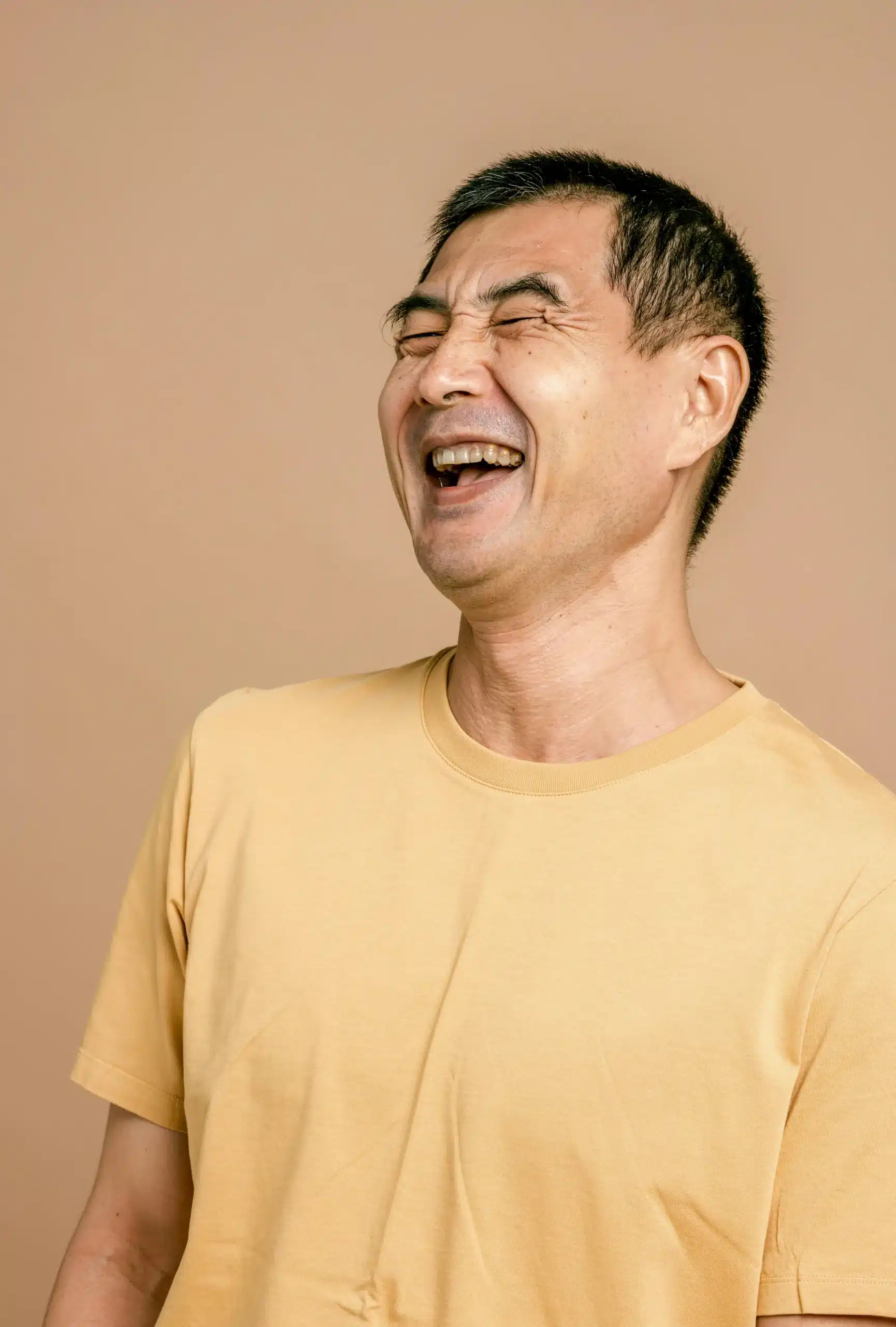 Asian man smiling and laughing warmly, expressing joy and ease in a candid moment of connection and lighthearted calm, soft