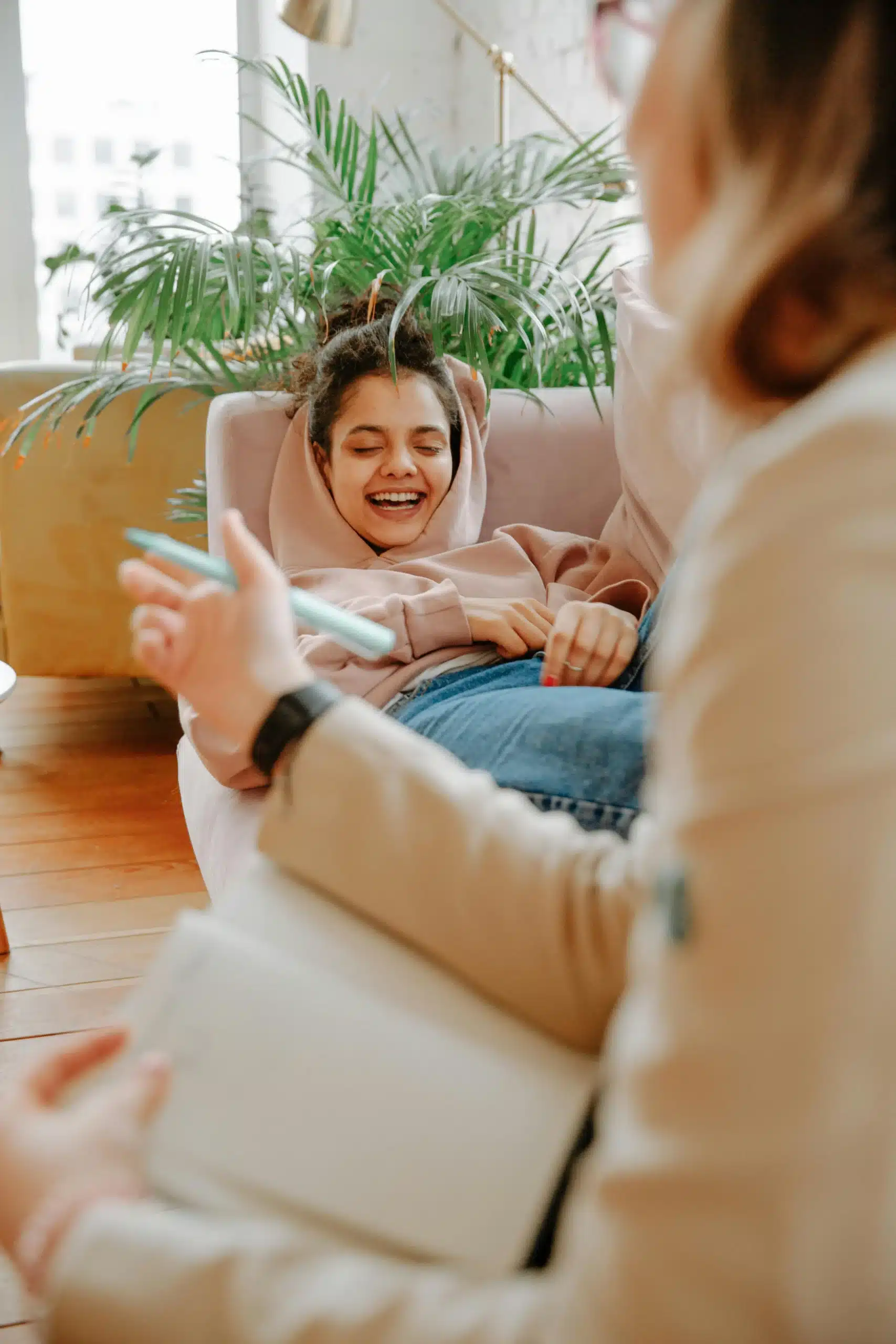  A girl laughing on a sofa while a therapist takes notes, reflecting connection, trust, and a safe healing space.
