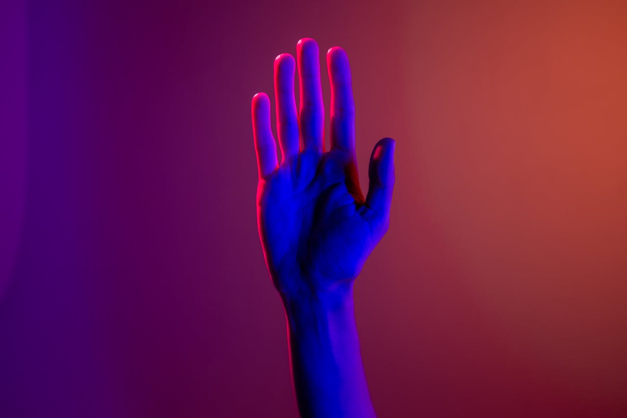 Hand raised in soft neon lighting symbolizing safety and awareness in trauma informed therapy