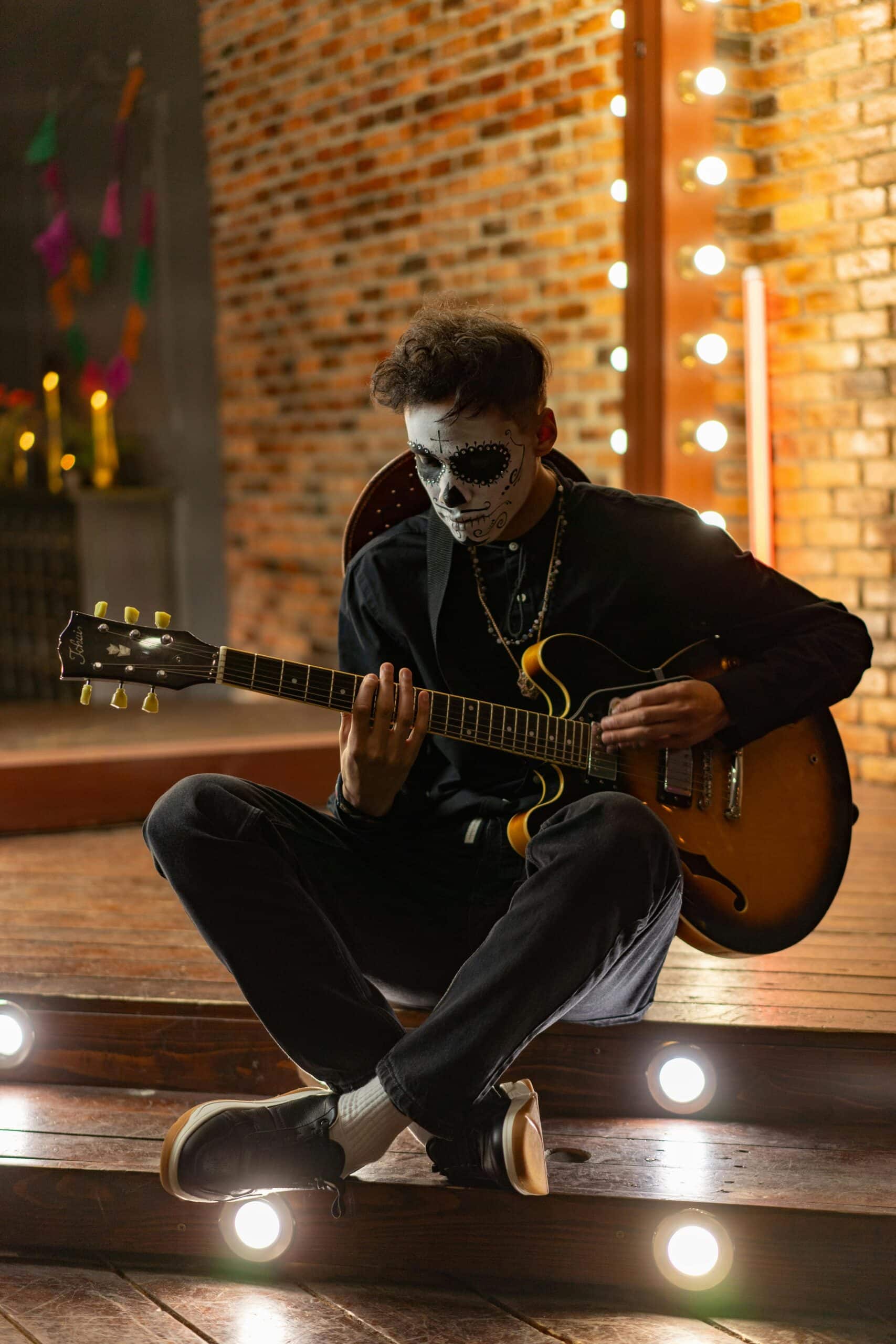A man with a painted face playing guitar, expressing individuality, creativity, and emotional release through music.