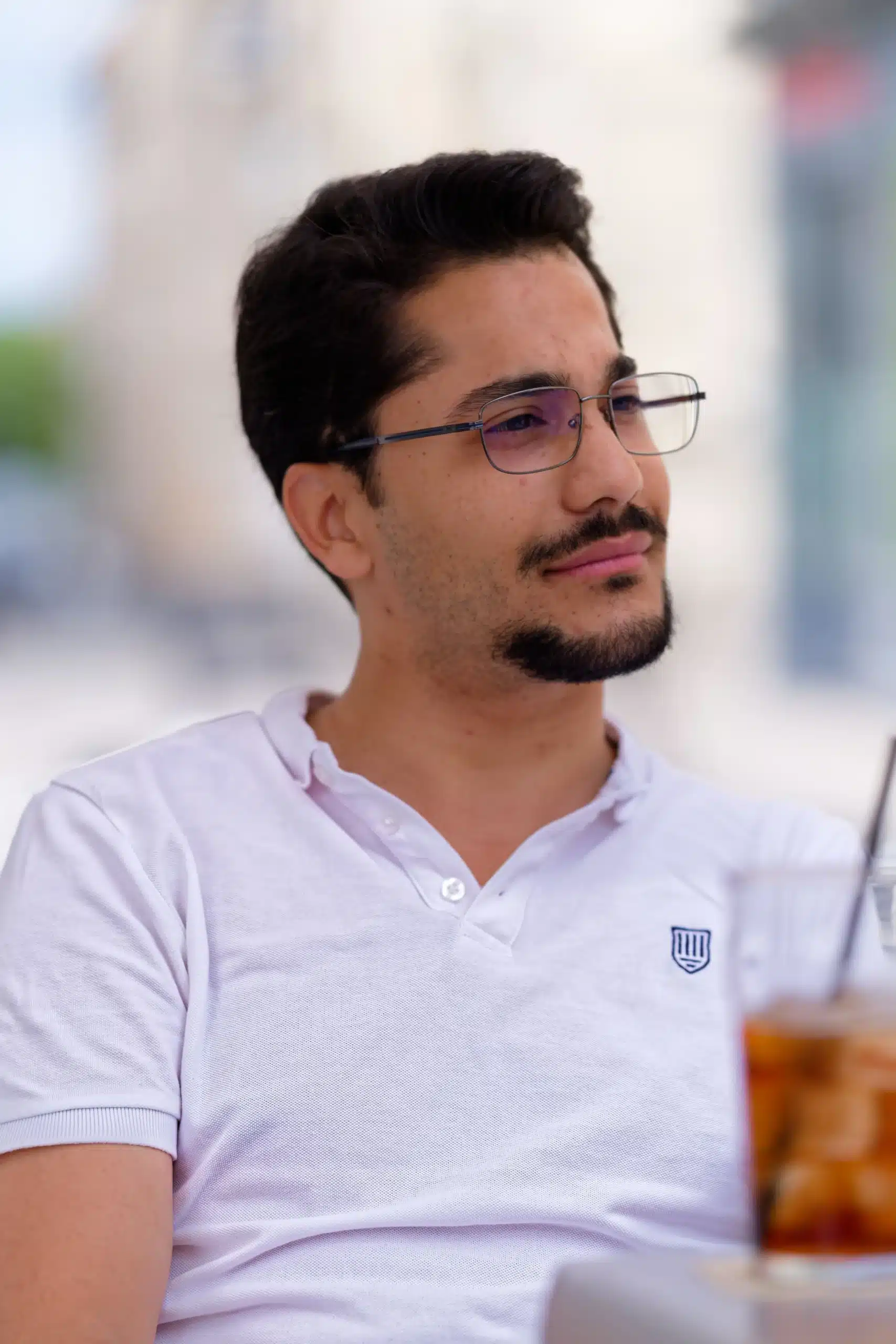 A young man wearing glasses and a white polo shirt looking thoughtful