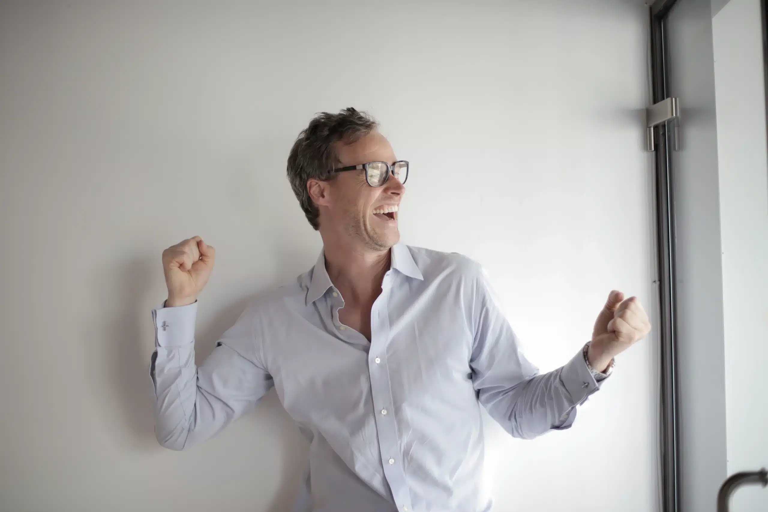 A smiling businessman in glasses celebrates a victory indoors, exuding positivity and joy