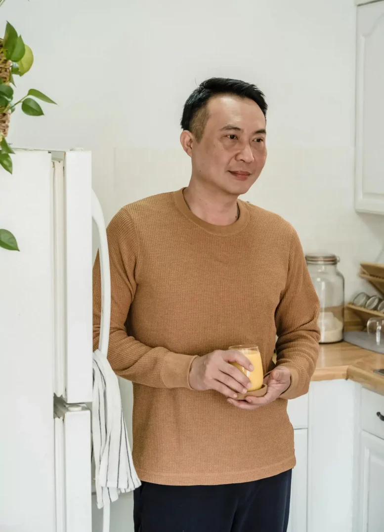 Asian man holding a glass of orange juice, looking peaceful and relaxed, embodying stillness, presence, and quiet contentment
