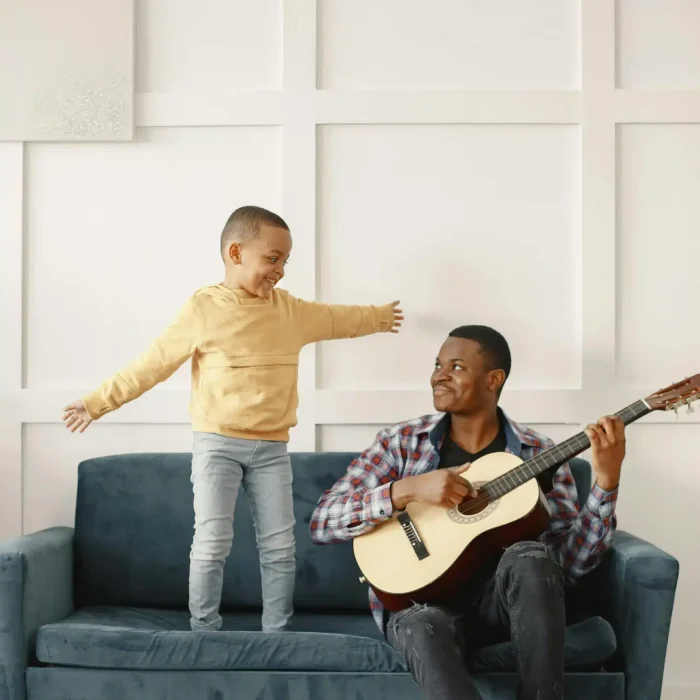  African American father playing guitar while son dances joyfully expressing connection rhythm and shared happiness time