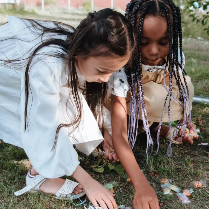 Two children picking up candies from the grass outside