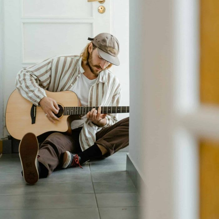 A man sitting on the floor playing guitar, reflecting focus, creativity, and emotional expression through music.